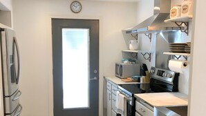 Ett modernt kök med vitvaror i rostfritt stål, en klocka på väggen och en hängande lampa.