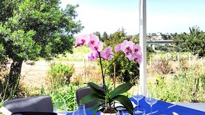 Ein Tisch für zwei, gedeckt mit einer blauen Tischdecke, weißen Tellern, Besteck und einem Blumentopf mit rosa Blüten.