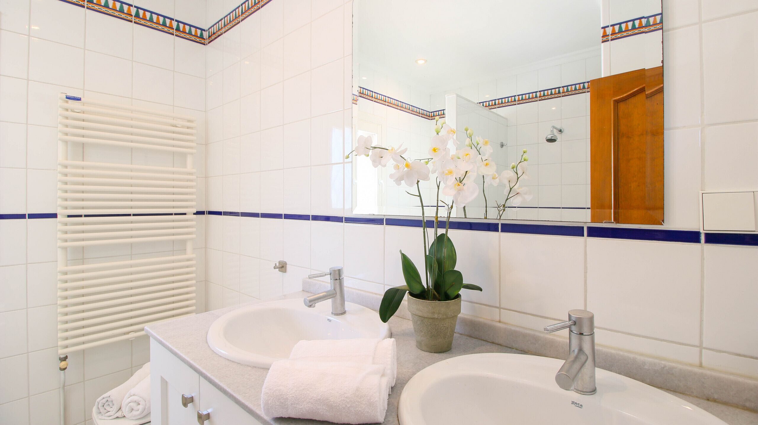 Un baño con dos lavamanos, un perchero para toallas, una planta en maceta y un espejo.