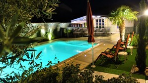 Une piscine dotée d’une terrasse carrelée, entourée de verdure et agrémentée d’un palmier.