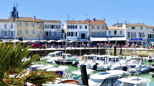 Un port de plaisance avec des bateaux amarrés, une promenade en bord de mer et des bâtiments abritant des commerces.