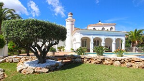 A white building with a tower, surrounded by a well-maintained garden with rocks and a large tree. - Luxurious Villa with air conditioning and pool Marquesa GU 6 People (Denia)