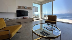 Un salon moderne doté d’un grand téléviseur, de sièges confortables, d’une table basse en verre et offrant une vue sur l’océan.