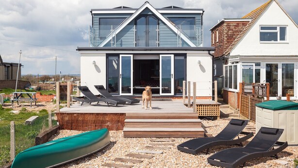 Een modern huis met twee verdiepingen, een terras, zitplaatsen buiten en een boot.