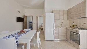 Una cocina moderna con un refrigerador, estufa y horno blancos, una mesa de comedor con sillas y un televisor montado en la pared.