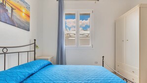 Un dormitorio con cama, armario, ventana con vista al cielo y un cuadro en la pared.