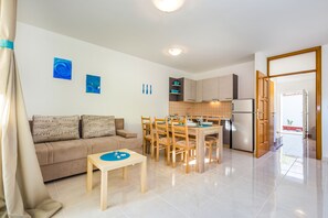 Un salon moderne comprenant un canapé, une table à manger et des chaises. Il y a également un coin cuisine avec des placards et un réfrigérateur.