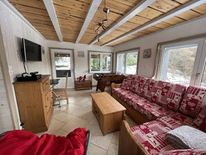 A cozy living room with a wooden ceiling, a sofa, a coffee table, a TV, and a foosball table.