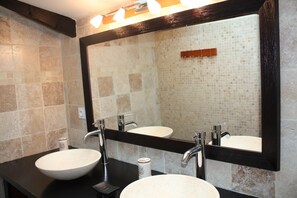 Une salle de bain avec deux lavabos, un grand miroir et un mur recouvert de carreaux.