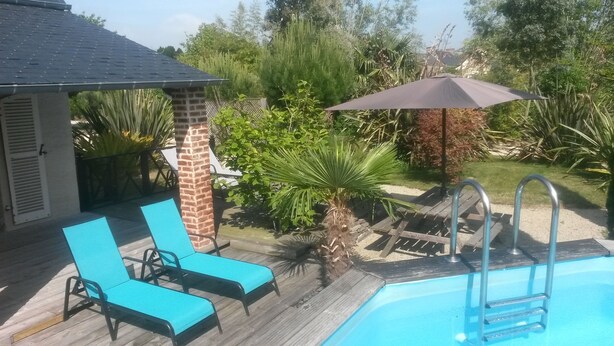 A backyard with a swimming pool, two blue lounge chairs, a brick pillar, and a wooden deck.
