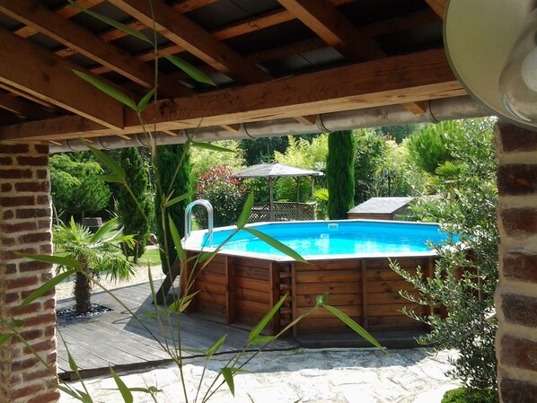 Un bain à remous en bois, installé sous une pergola, avec une piscine en arrière-plan.