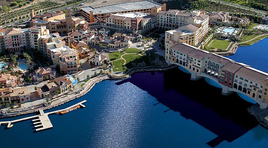 Vista aérea de un complejo turístico costero con varios edificios, un puerto deportivo y una gran extensión de agua.