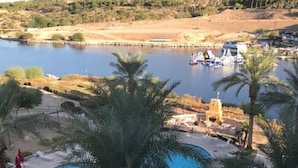 Zona de piscina con palmeras, vista a un río y montañas al fondo.