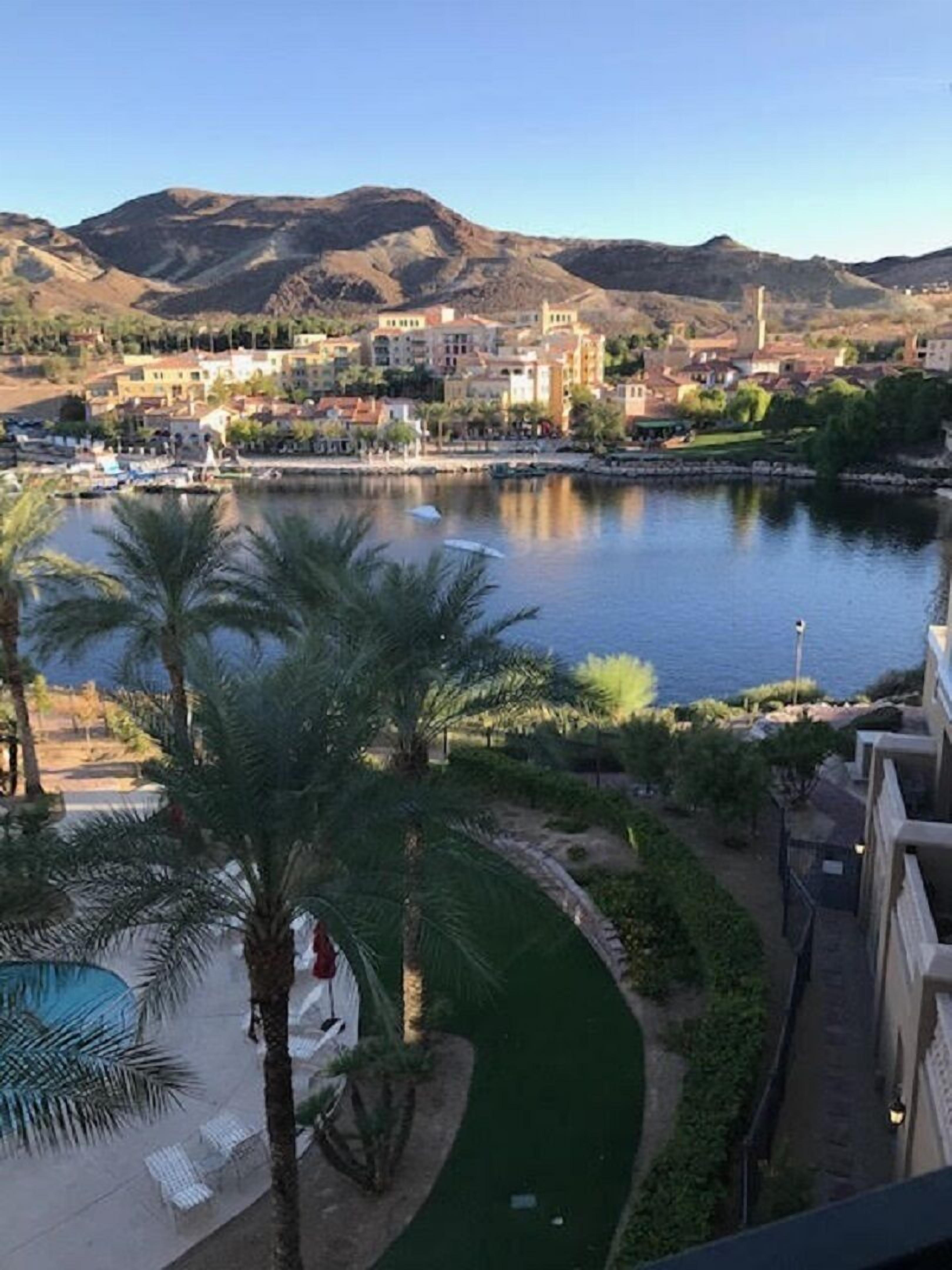 A view of a waterfront property with a pool, palm trees, and a mountain backdrop.