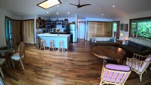 A spacious living area with a central island, wooden flooring, a dining area with chairs, a sofa, and a ceiling fan. - Private beach front property, the perfect getaway! Enjoy our slice of paradise. (Waimea)