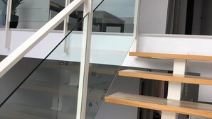 Una escalera moderna con barandillas de vidrio y peldaños de madera, que conduce a un piso superior.