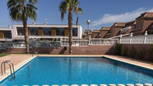 Una piscina rectangular con agua azul cristalina, rodeada por una valla blanca y palmeras.