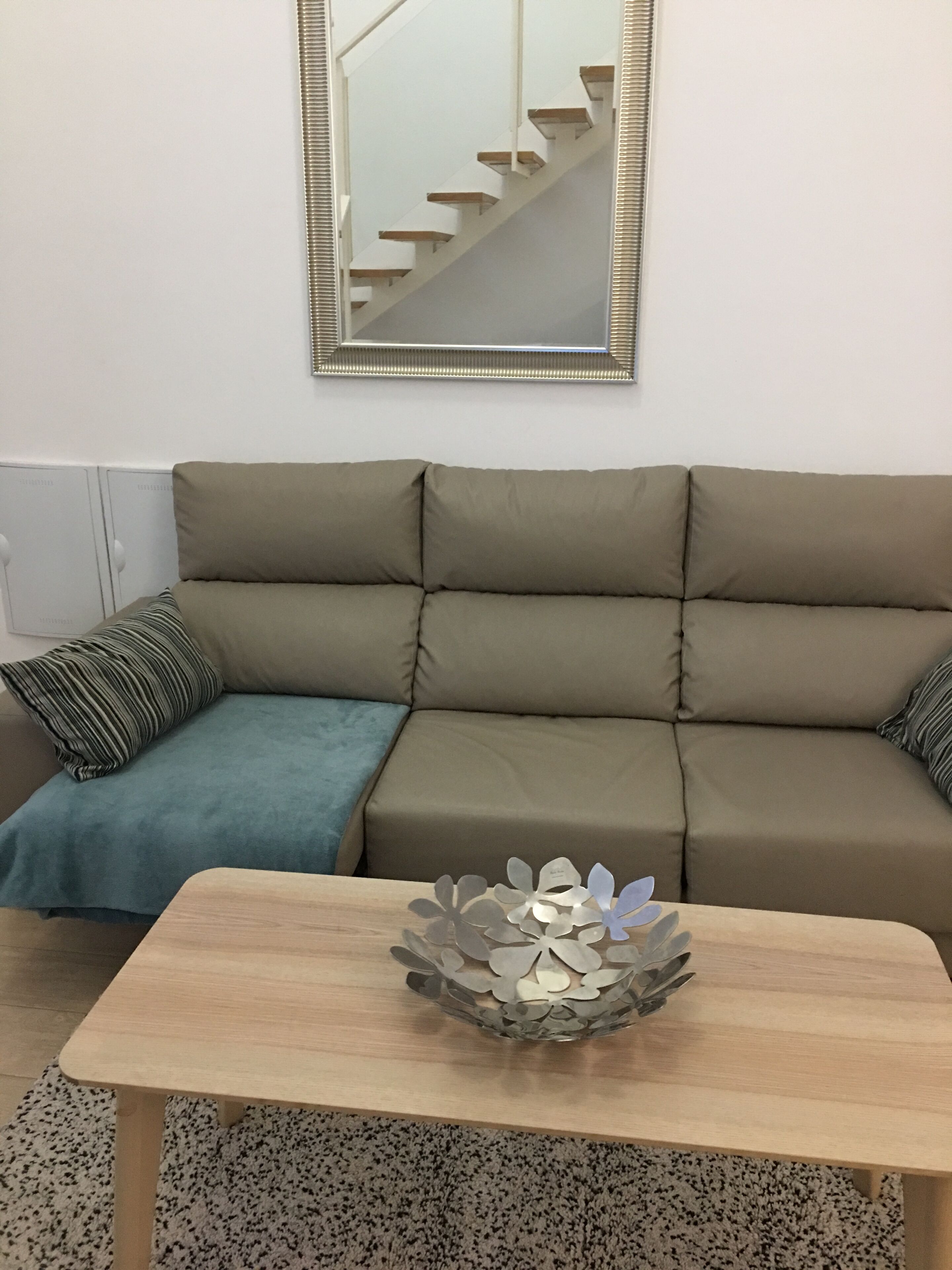 A living room with a sofa, a coffee table, a striped pillow, a blue throw blanket, and a mirror on the wall.