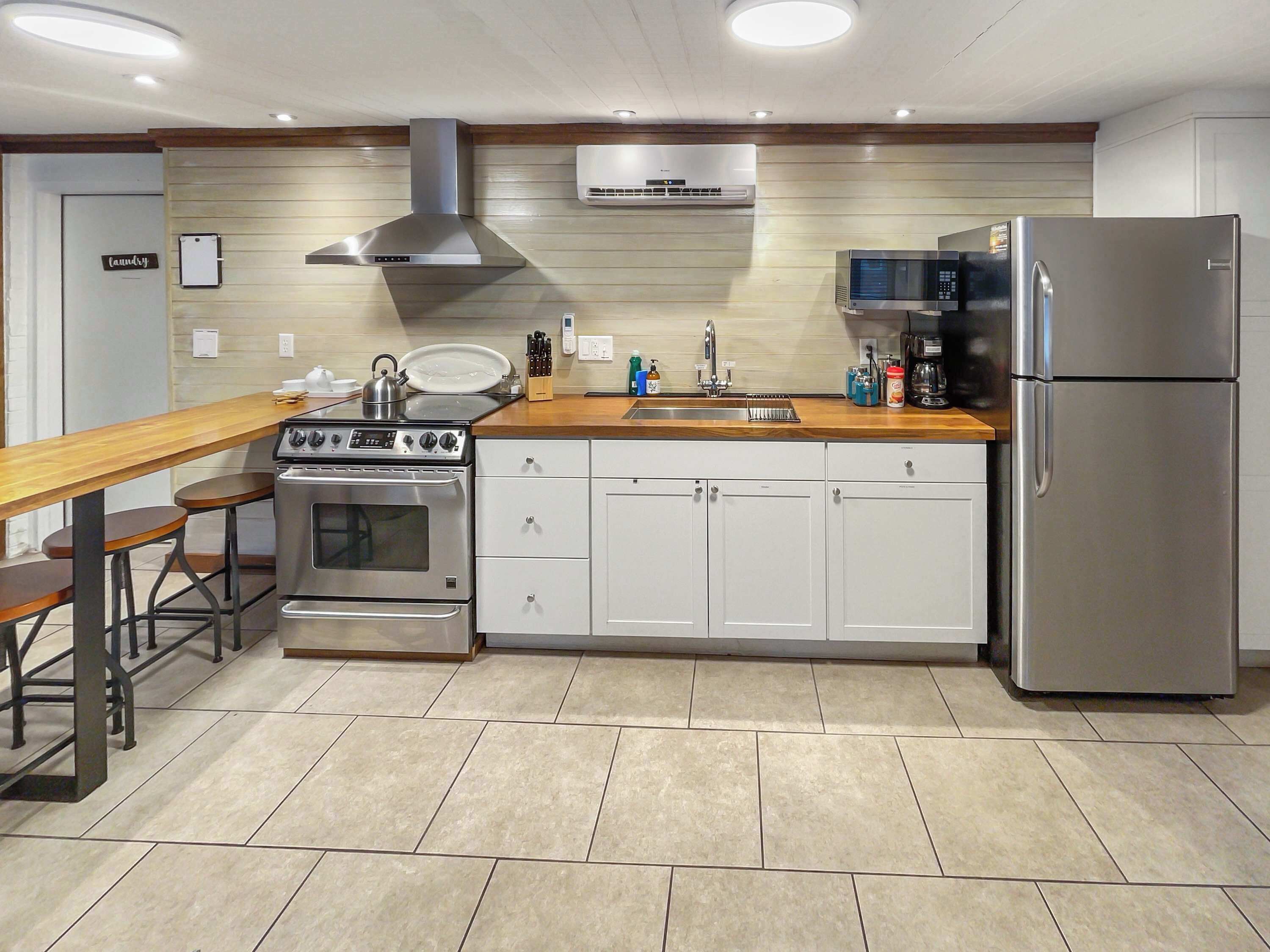 A modern kitchen with a stainless steel stove, oven, and refrigerator, wooden countertop, and white cabinets.