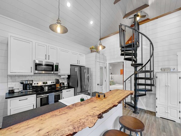A modern kitchen with white cabinetry, stainless steel appliances, a wooden island, and a spiral staircase.