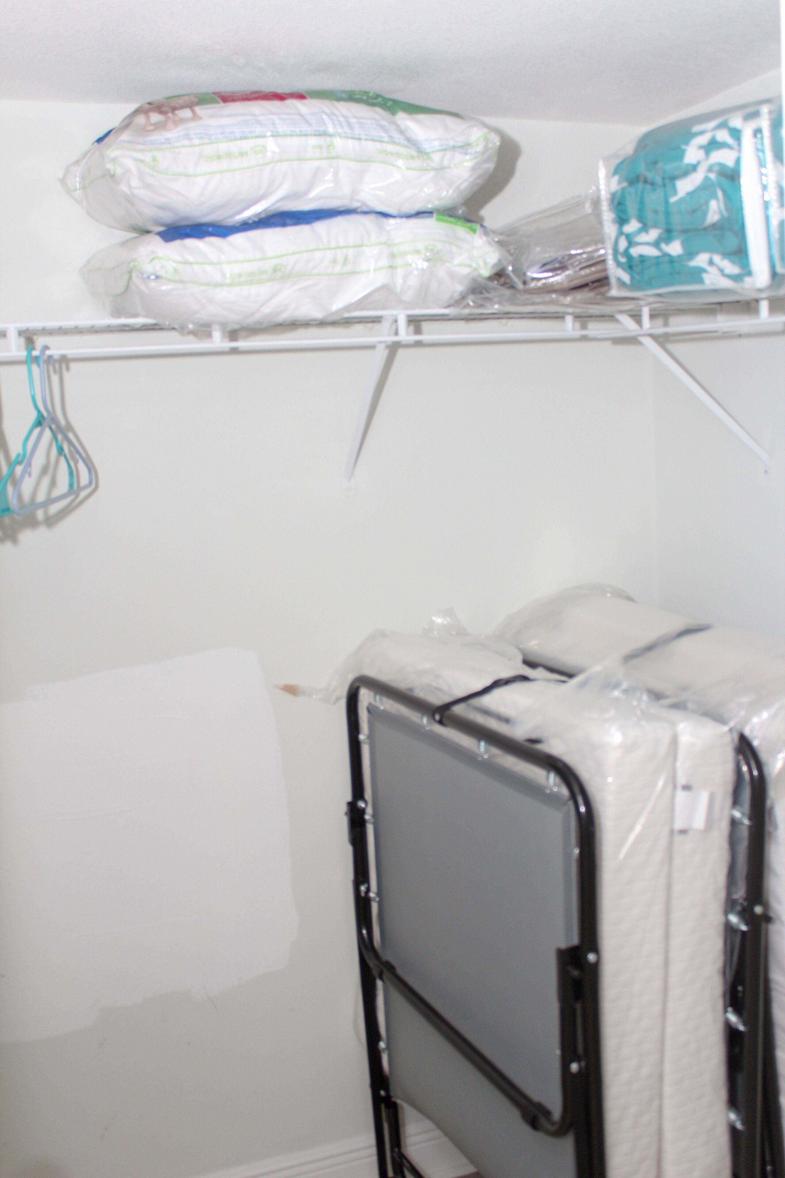 A storage area with shelves holding bags and a metal rack with a mattress.