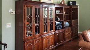 Un salón amplio con un gran armario de madera, un cuadro enmarcado en la pared y un sillón de cuero.