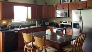 Una cocina con armarios de madera, una isla central con sillas, un ventilador de techo y un refrigerador.