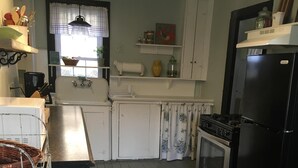 A kitchen with white cabinets, a black refrigerator, a striped rug, and a hanging light fixture. - StarField Cottage...The Perfect Cooperstown Dreams Park Getaway! (Cooperstown)