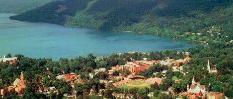 Vista aérea de un pueblo con un lago, rodeado de bosques densos y colinas.