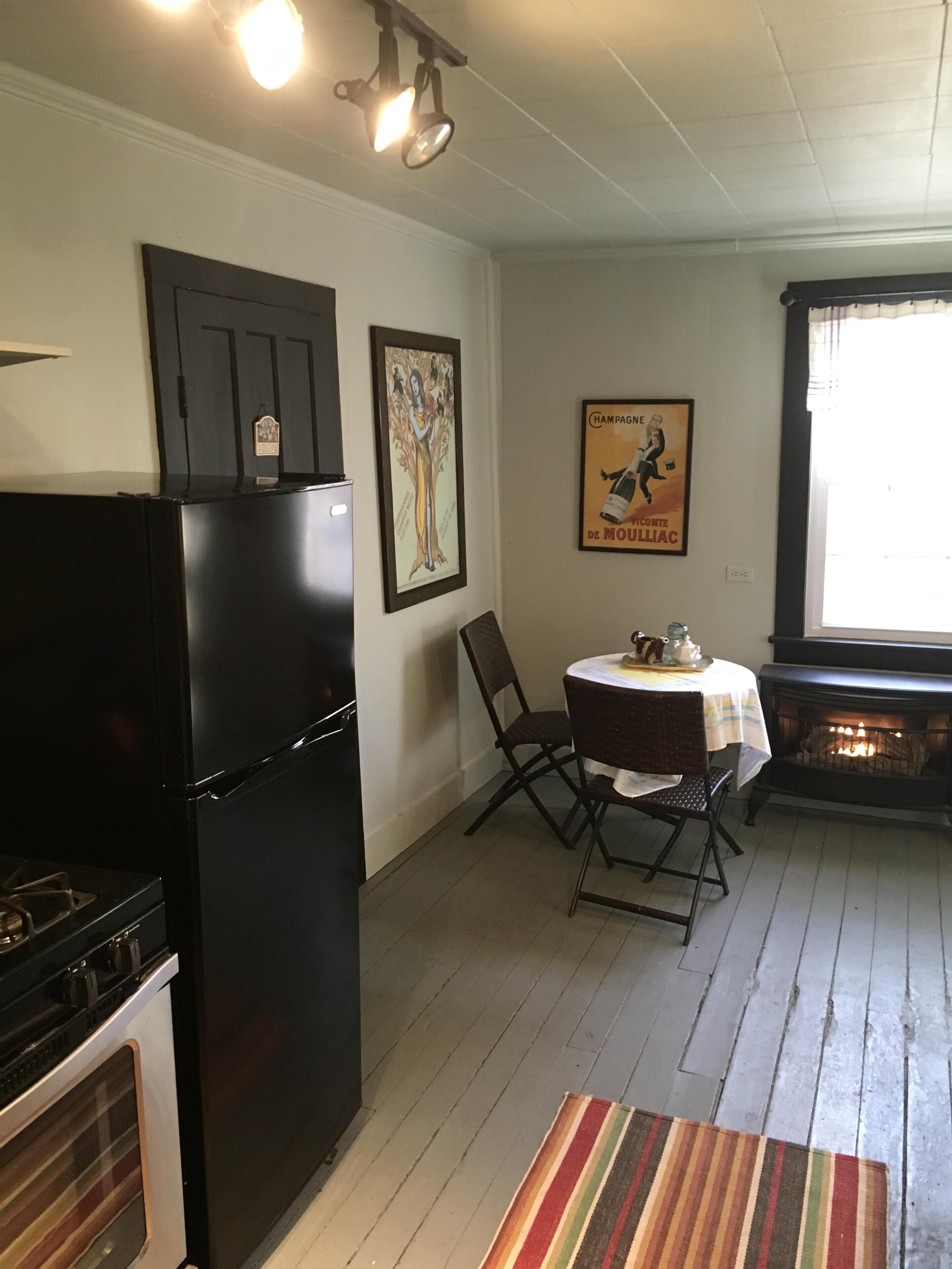 A kitchen with a black refrigerator, a stove, a dining table with chairs, and a fireplace.