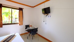 Habitación de hotel con cama, una mesita con dos sillas, televisión montada en la pared y ventana con cortinas.
