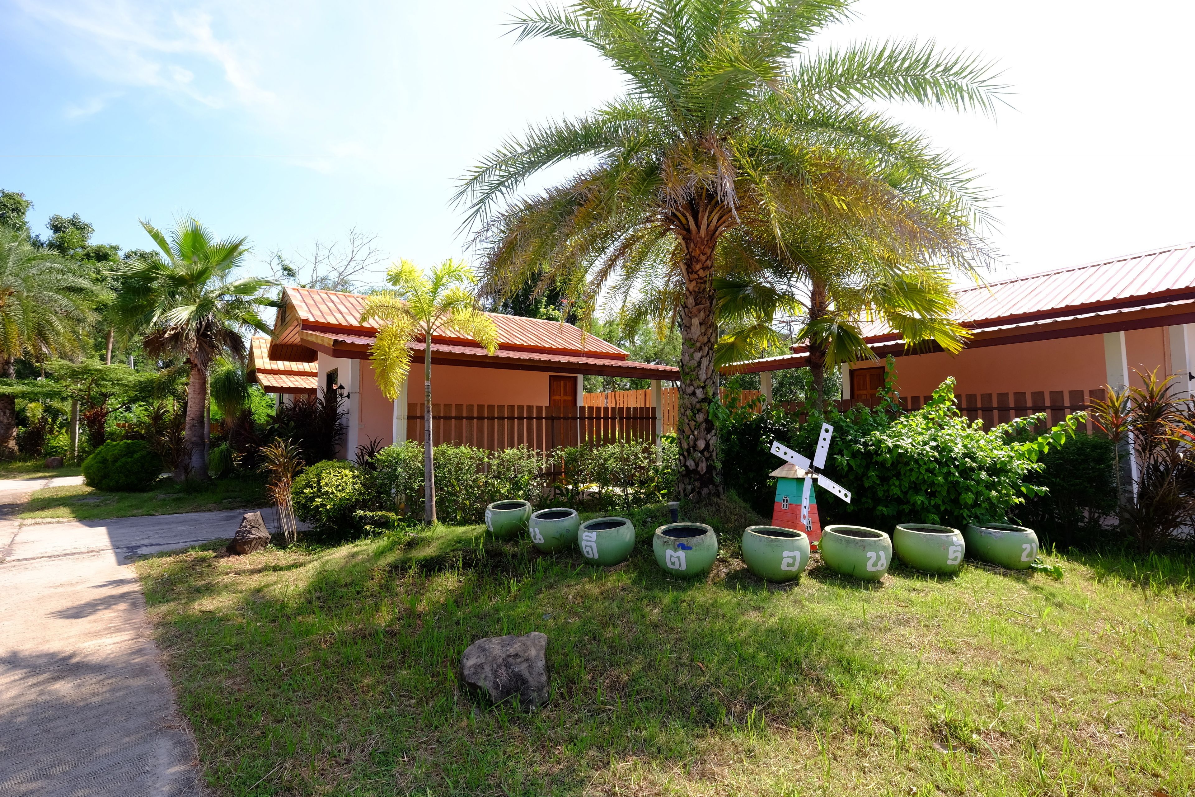 A building with a red roof and a palm tree in the front yard. There are green planters with numbers on them.