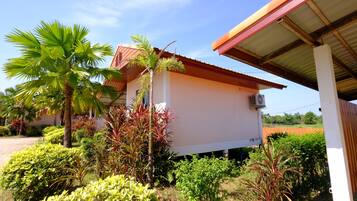 Un edificio de paredes blancas y techo rojo, rodeado de diversas plantas y una palmera.