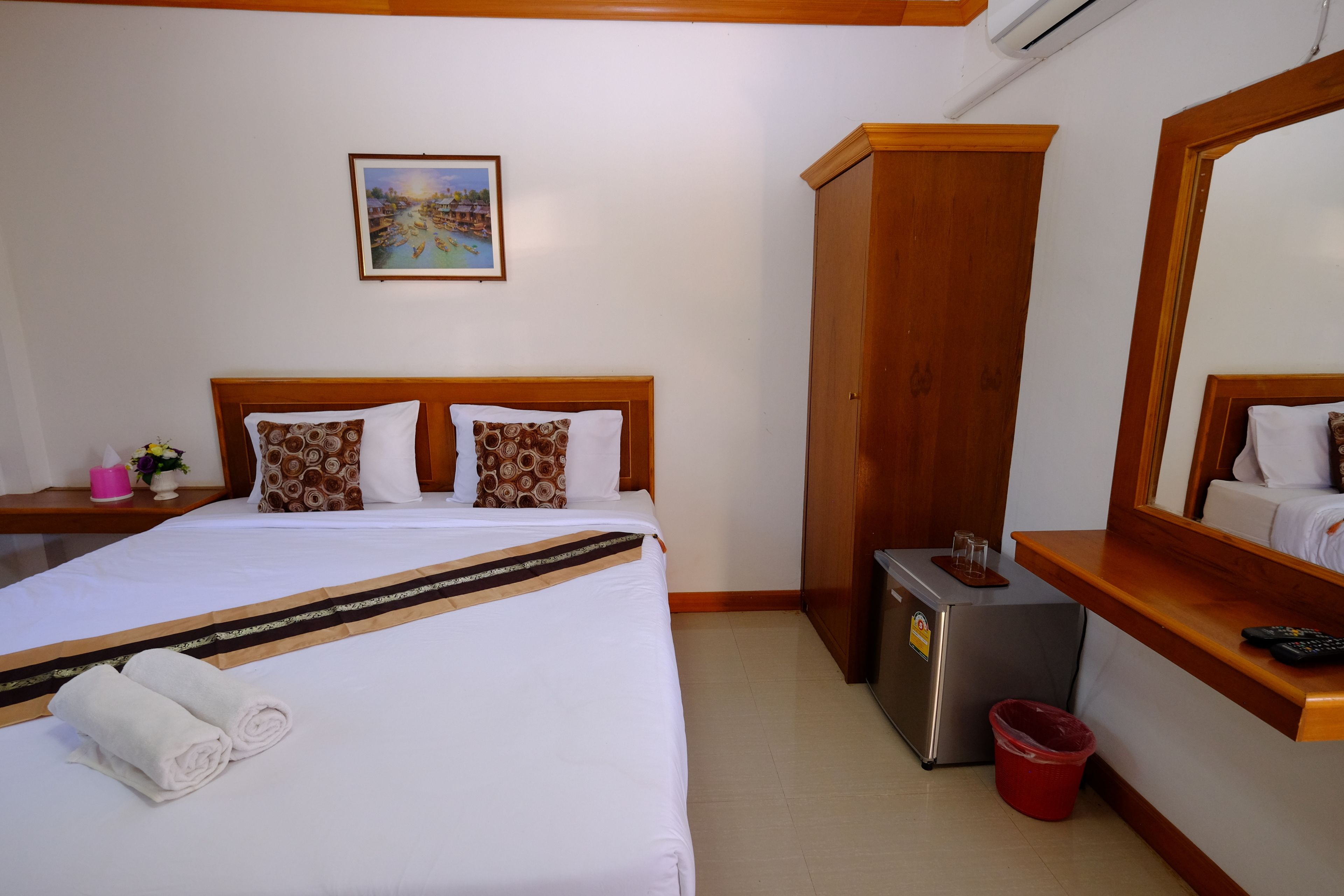 A neatly made bed with a patterned bedspread, a small table with a remote control, a trash bin, and a wall-mounted air conditioning unit.
