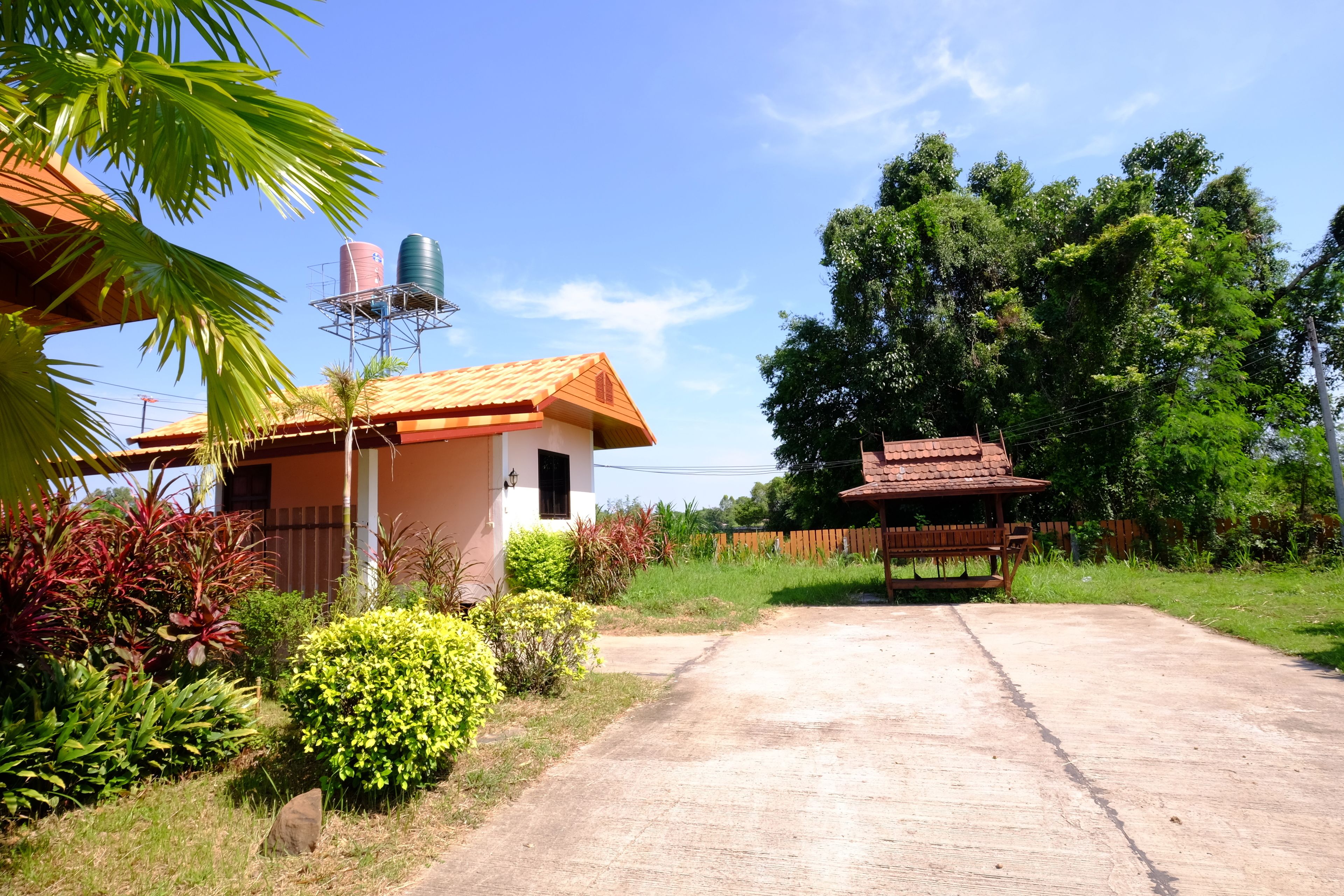 A residential property with a paved driveway, a small house with a tiled roof, and a water tank on a metal structure.