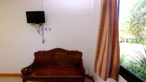 Un banco de madera en una habitación con un televisor montado en la pared y una ventana con cortina.