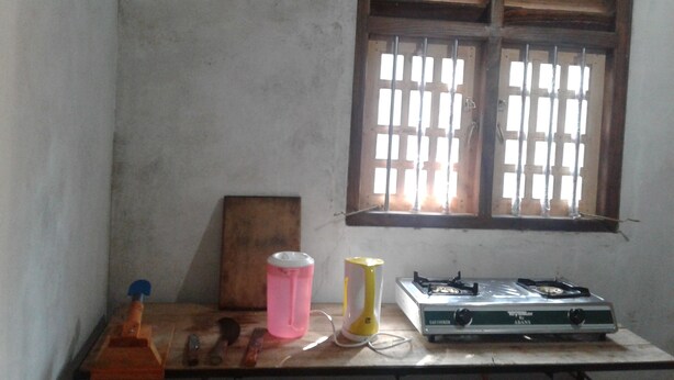 A kitchen with a gas stove, a window with bars, and various utensils on a wooden table. - Patana holiday home (Kotapola)