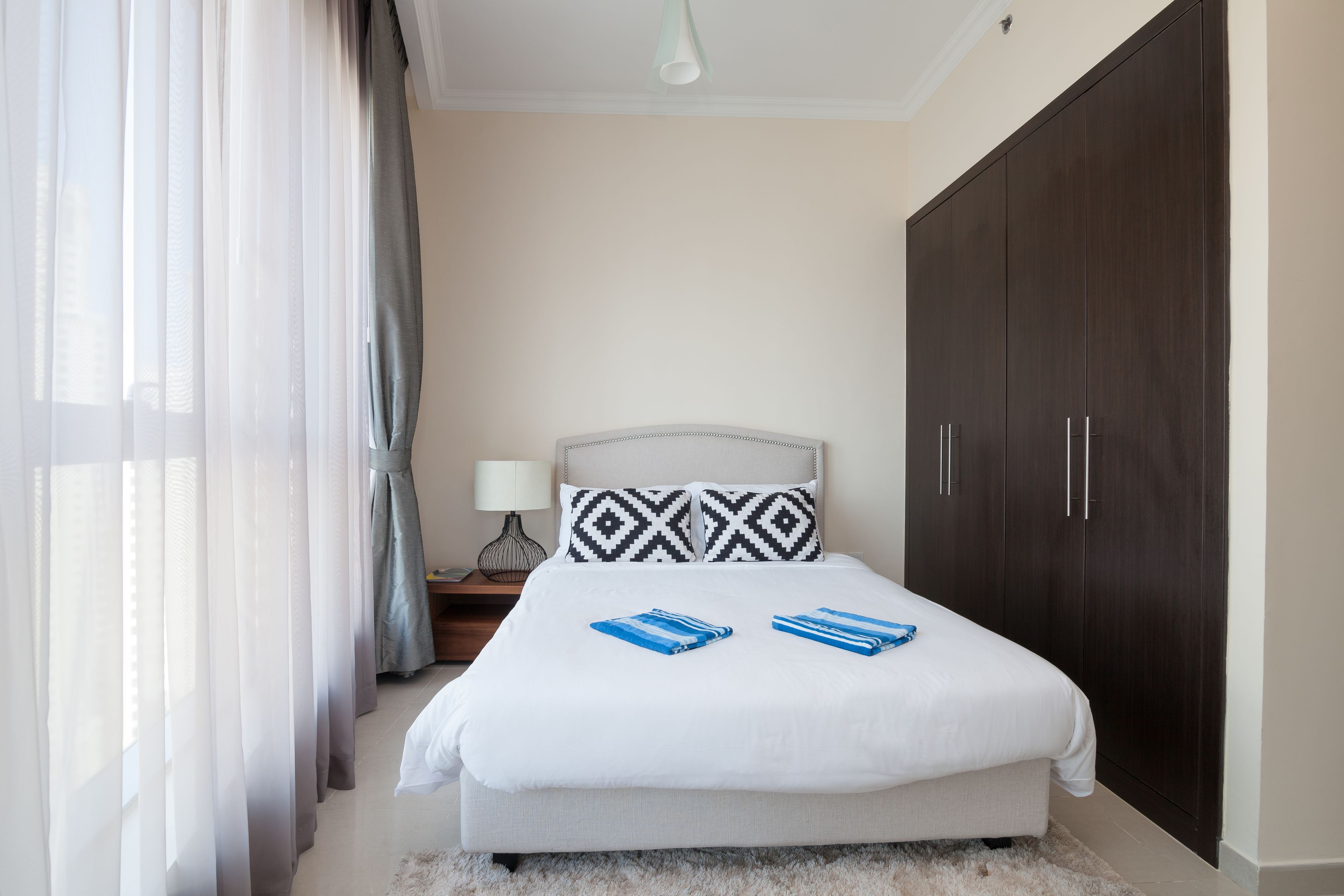 A bedroom with a bed, a wardrobe, a nightstand, and a lamp.