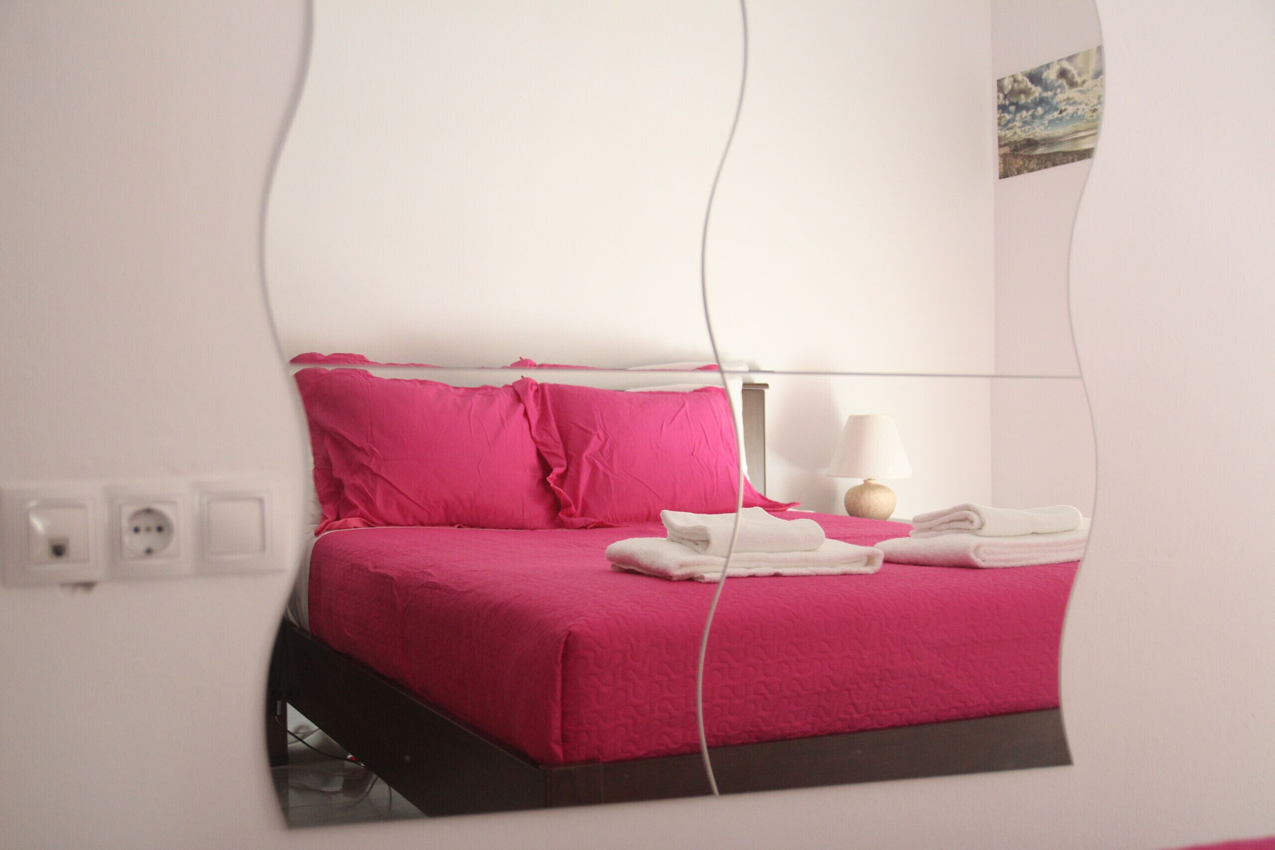 A mirrored view of a bed with pink bedding, a bedside lamp, and neatly folded white towels.