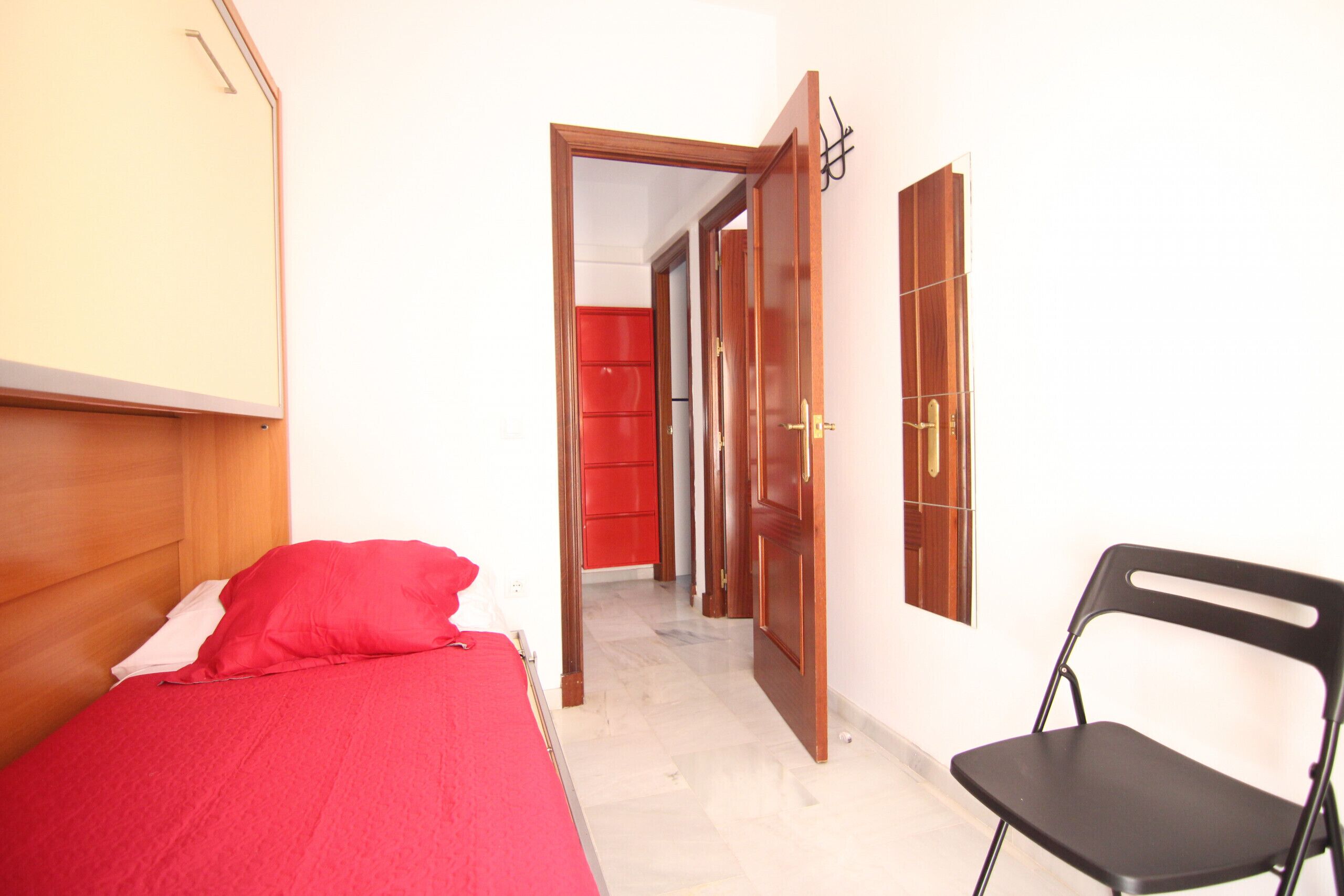 A room with a bed, a chair, and a door leading to another room.