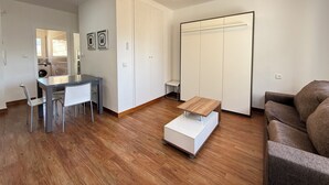 A modern living room with a wooden floor, a ceiling fan, a dining table with chairs, a sofa, and a wardrobe. - Agi Josep Sabate 42 Apartamento for rent in Roses Girona. (Rosas / Roses)