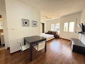 A modern living room with a dining table, two chairs, a sofa, and a TV.