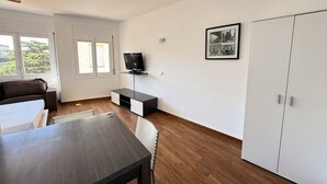 A room with a dining table, a sofa, a TV on a stand, a wardrobe, and a window with blinds. - Agi Josep Sabate 42 Apartamento for rent in Roses Girona. (Rosas / Roses)