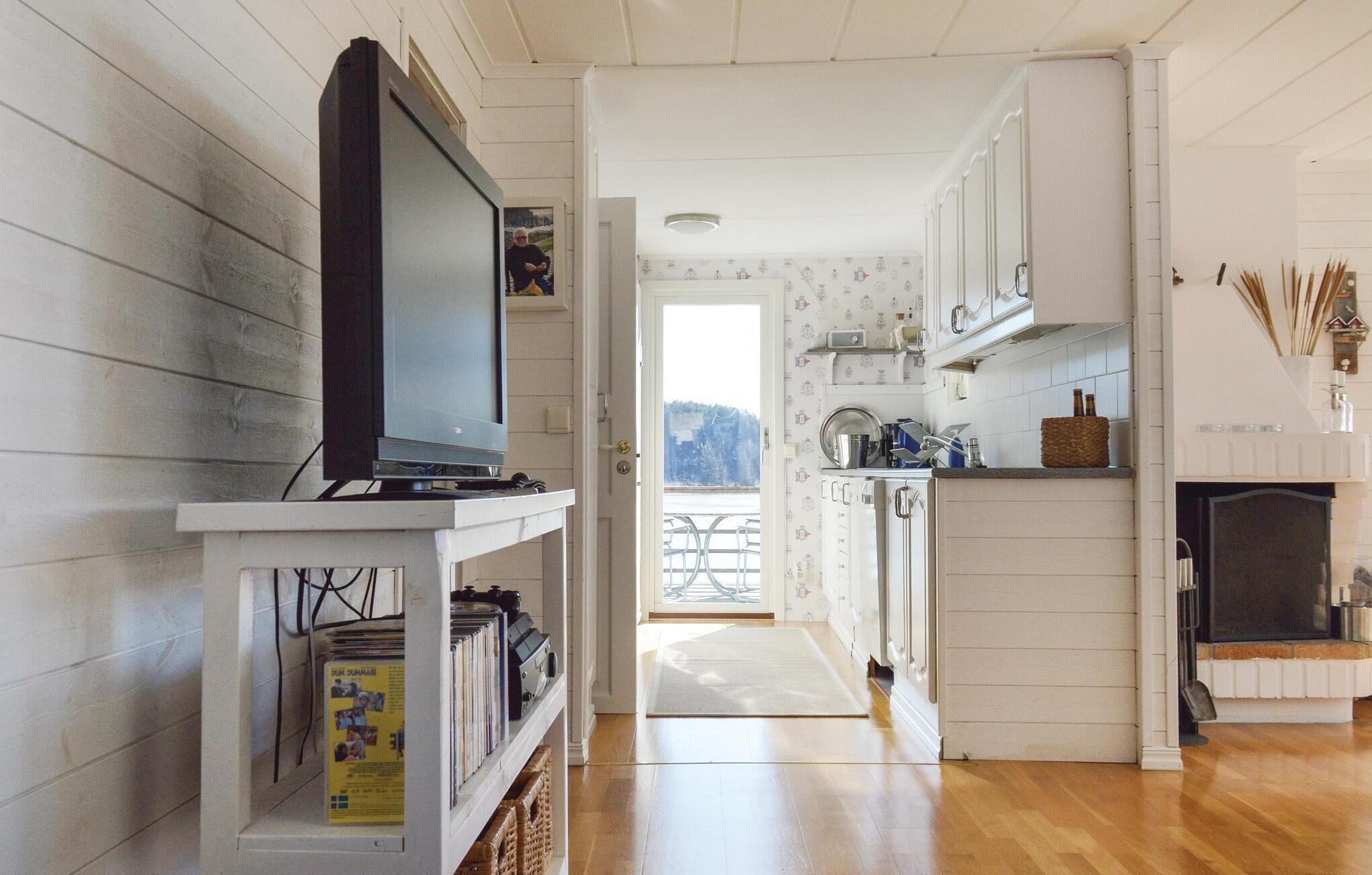 Ett kök med vita skåp, en tv på ett tv-bord och utsikt mot omgivningen.