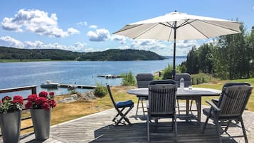 En träaltan med ett bord och stolar, ett parasoll och krukväxter.