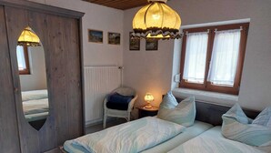 A bedroom with a bed, a chair, a lamp, and a window with curtains. - Ferienwohnung, 55 qm, 2 Schlafzimmer, Balkon und Terrasse (Siegsdorf)