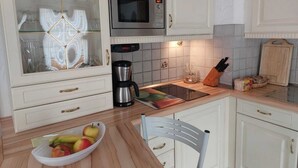 A kitchen with white cabinets, a microwave, a coffee maker, and a fruit bowl on the counter. - Ferienwohnung, 55 qm, 2 Schlafzimmer, Balkon und Terrasse (Siegsdorf)
