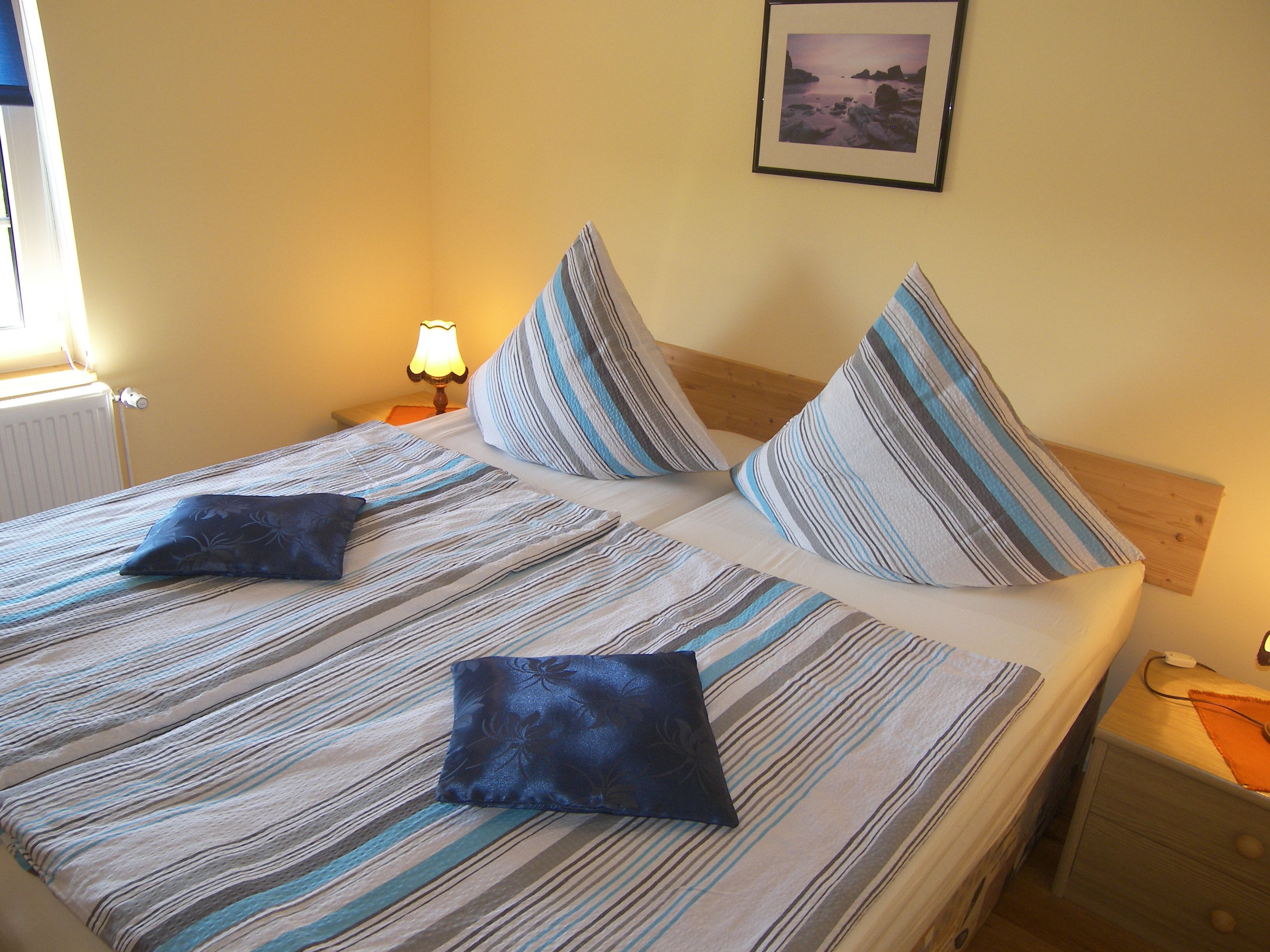 Un letto matrimoniale con lenzuola a righe e due cuscini, un comodino con una lampada e un quadro appeso al muro.