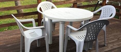Une terrasse en bois avec une table ronde et quatre chaises en plastique blanc.