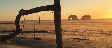 A wooden swing set on a sandy beach with a sunset in the background.